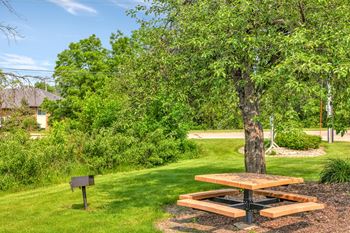 A picnic table sits in the middle of a grassy area with a tree nearby.